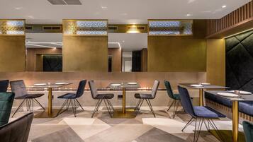 A modern restaurant with multiple tables and chairs, a central fire feature, and decorative panels.