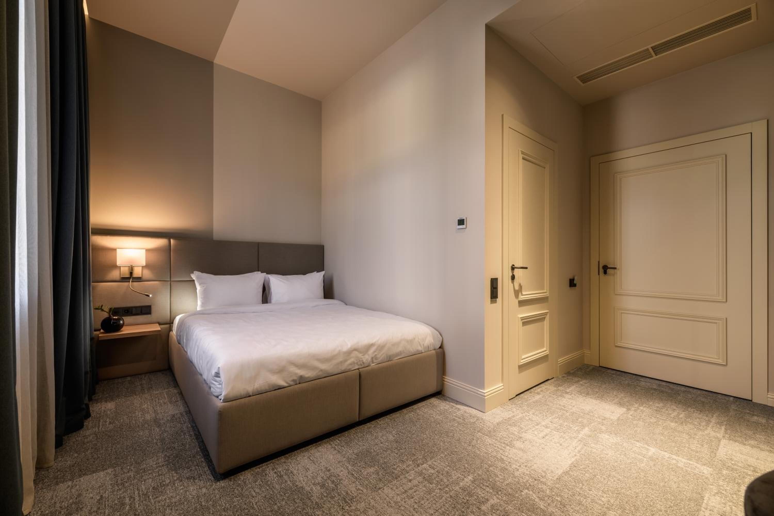 Un dormitorio con cama, mesita de noche, lámpara y puerta.