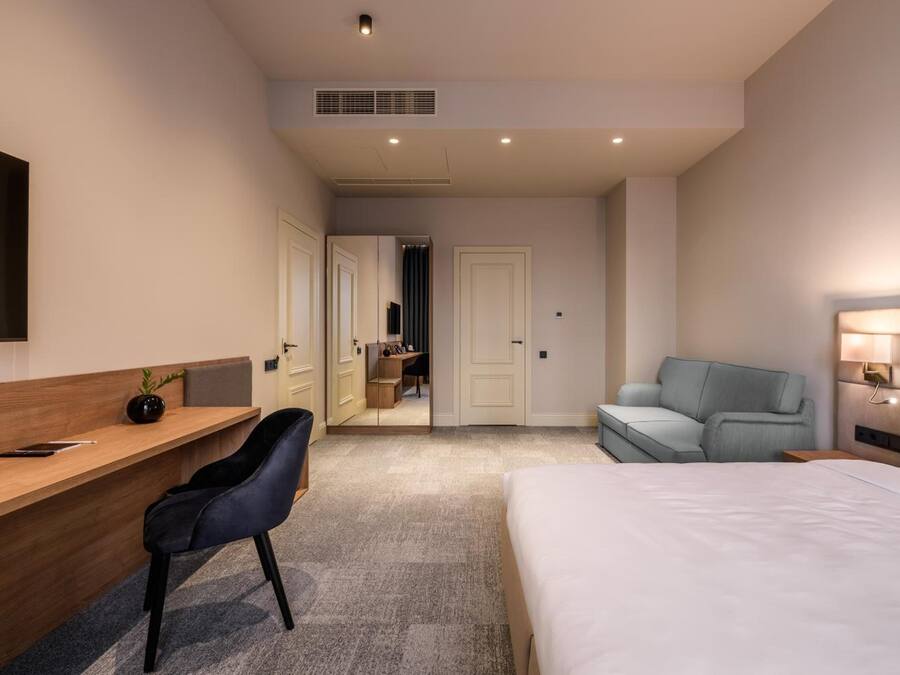 Quarto de hotel moderno com uma cama, uma mesa com cadeira, um sofá e uma TV fixada na parede.