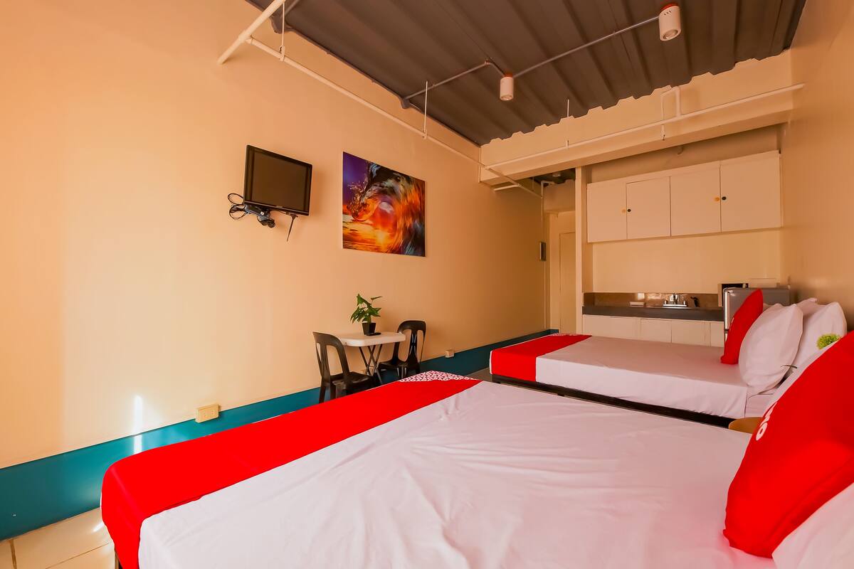 A hotel room with two beds, a small table with chairs, a TV, and a painting on the wall.