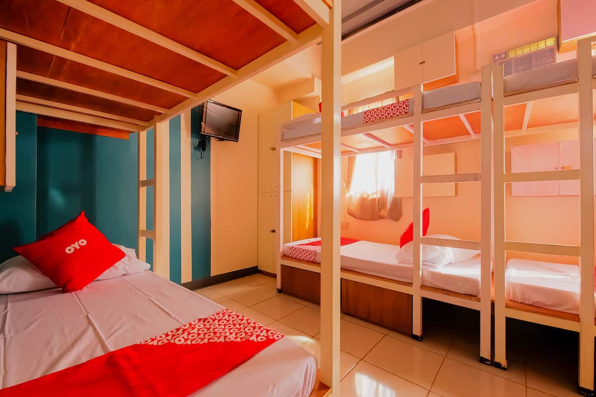 A room with bunk beds, a television, and a bed with red pillows.