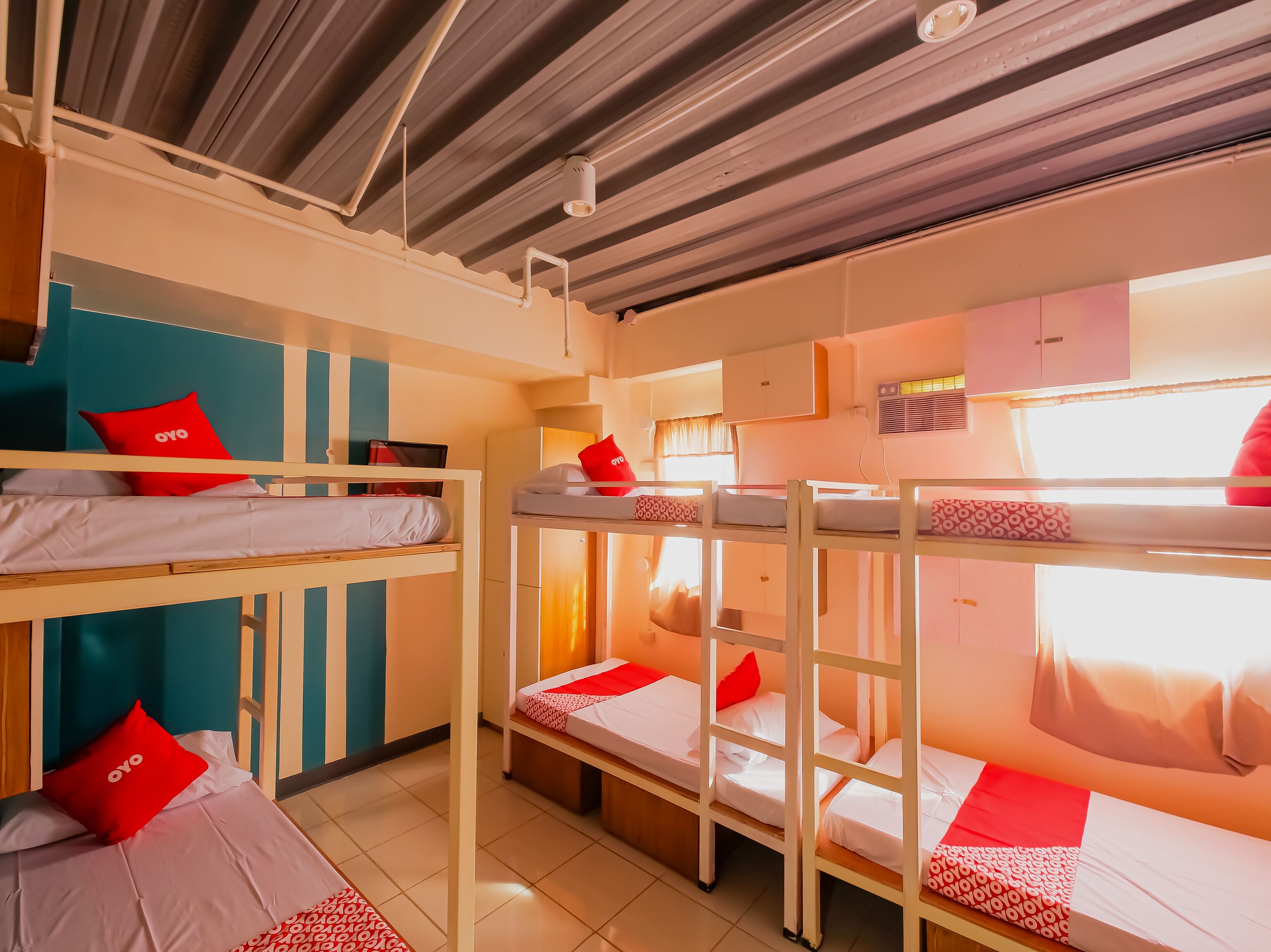 A dormitory room with bunk beds, a window with curtains, and an air conditioning unit on the wall.