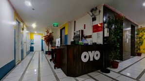 Een hotel receptie met een receptiebalie met de aanduiding 'OYO', een klok en een bord met inchecktijden.