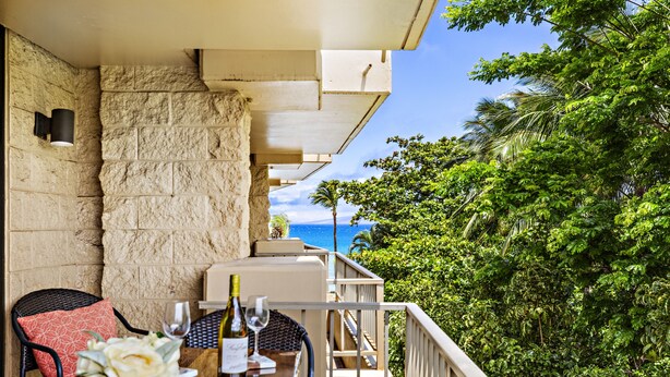 A balcony with a table set for dining, a stone wall, and a view of the ocean.