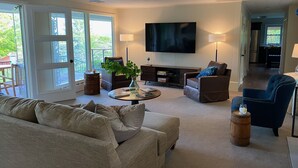 A spacious living room with a large flat-screen TV, comfortable seating, and a view of the outdoors.