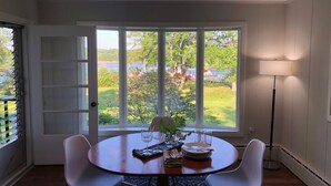 A dining area with a round table, white chairs, a vase with flowers, wine glasses, and a lamp.