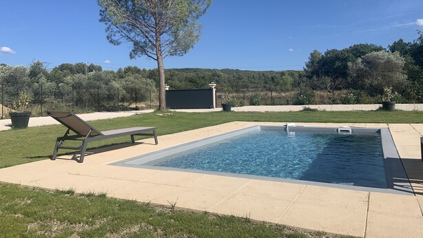 Piscina retangular com banheira de hidromassagem integrada, rodeada por um deck de concreto.