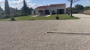Uma casa com telhado de azulejos, piscina e entrada com calçada de brita.
