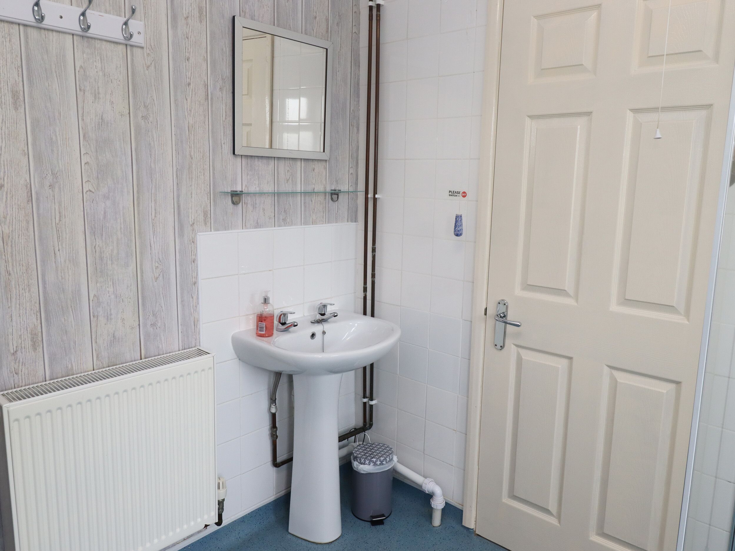 Une salle de bain avec un lavabo blanc, un miroir et une porte sur laquelle est apposée une pancarte indiquant : « Veuillez éteindre ».