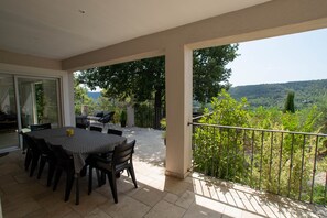 Une terrasse extérieure avec une table et des chaises, une porte vitrée donnant sur l’intérieur et une vue sur un paysage luxuriant.