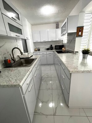 A modern kitchen with white cabinetry, a marble countertop, and a stainless steel sink.