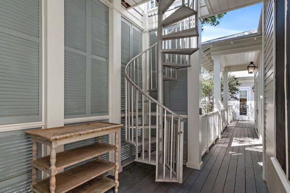 A wooden porch with a spiral staircase leading to a door, a small table, and a railing.