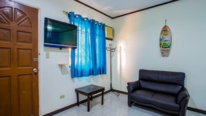 A living room with a TV mounted on the wall, a sofa, a small table, and a door. - OYO 814 Laurien's Budget Hotel (Tagaytay)
