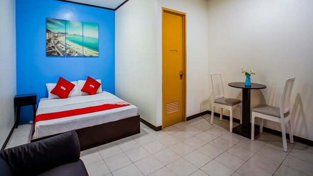 A hotel room with a bed, a painting of a beach, a door with a no-smoking sign, a small table with a vase, and two chairs. - OYO 814 Laurien's Budget Hotel (Tagaytay)