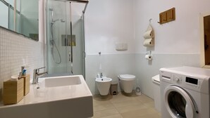 Un baño moderno con ducha envuelta en vidrio, lavamanos, inodoro y lavadora.
