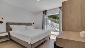 Un dormitorio moderno con una cama grande, una mesita de noche de madera, una mesita auxiliar y vistas a un balcón con escaleras.
