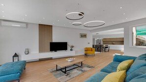 Una sala de estar moderna con un televisor de pantalla plana, un comedor con una silla amarilla, y una cocina visible al fondo.