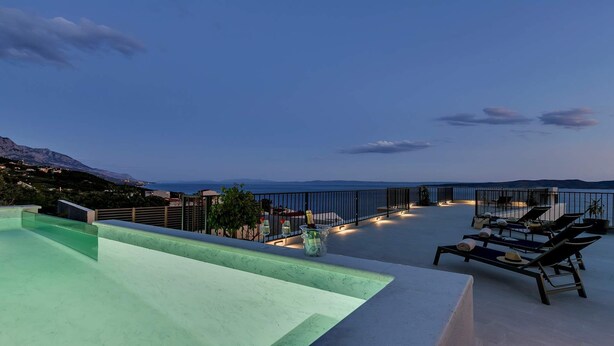 Una terraza en la azotea con piscina, sillones de descanso y vistas al mar y las montañas.