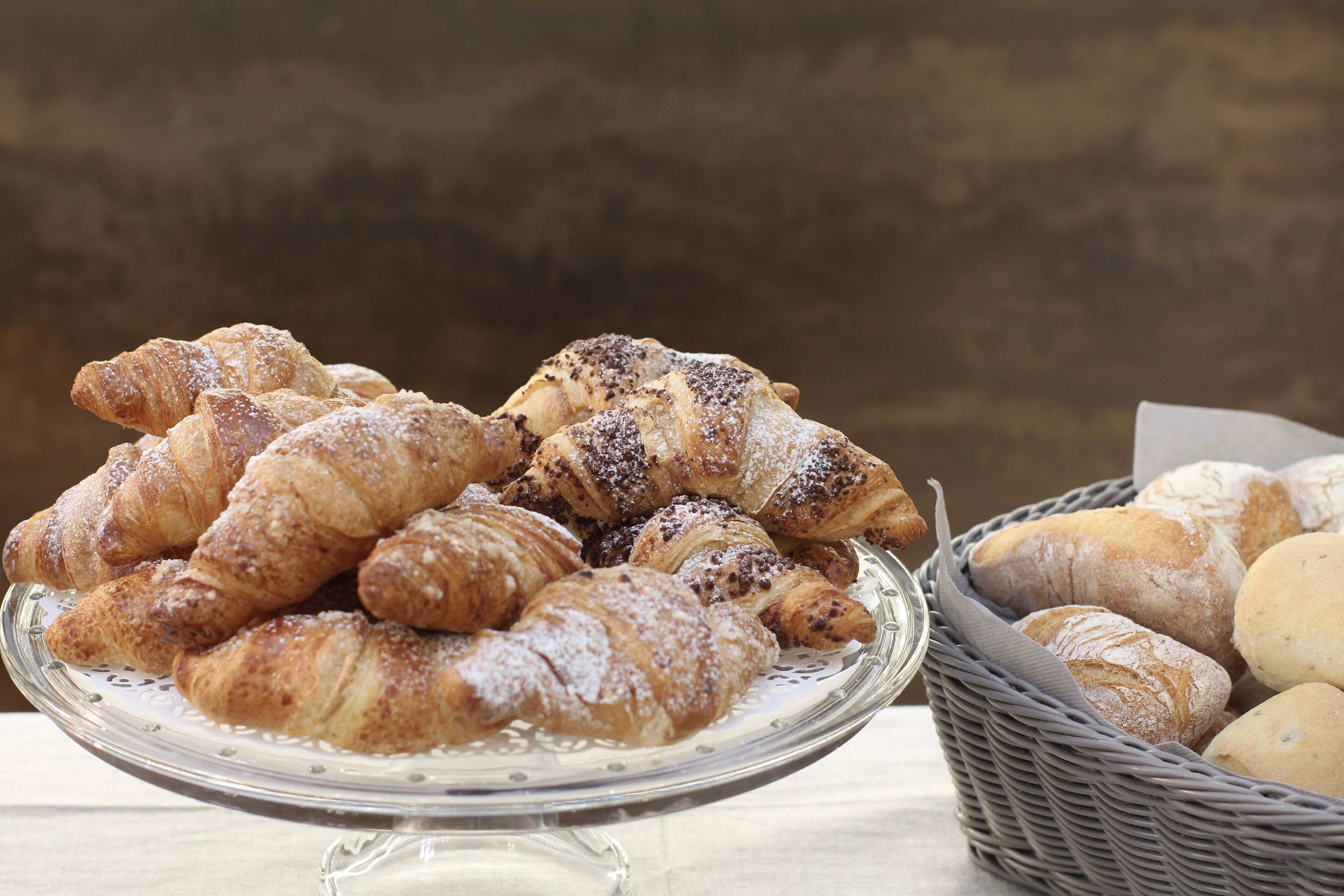 A glass display stand with a variety of pastries, including croissants and bread, on a table.