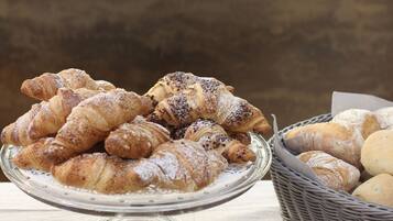 A glass display stand with a variety of pastries, including croissants and bread, on a table.