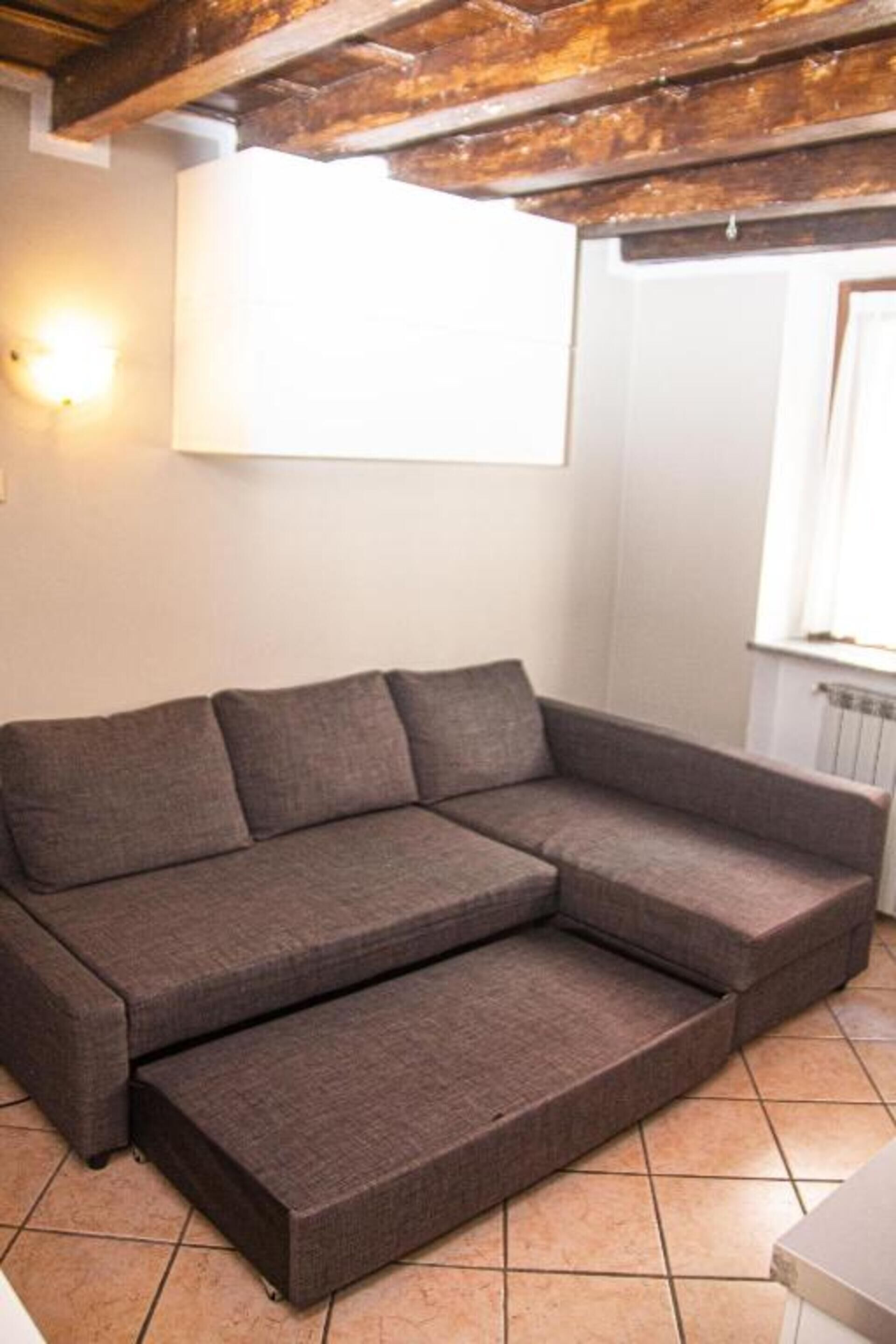 A sectional sofa in a room with a tiled floor, a wooden ceiling, and a wall-mounted light fixture.