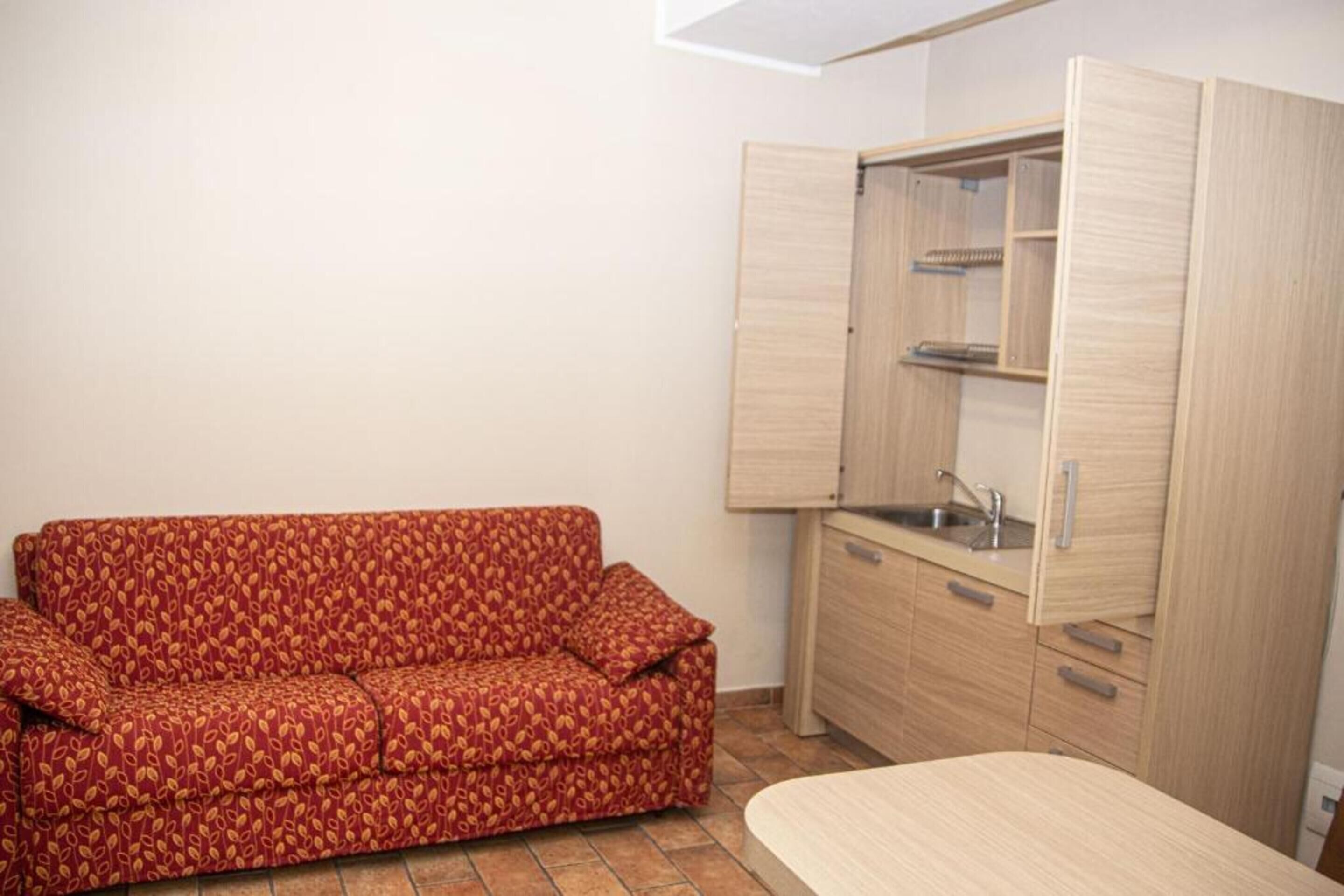 A small room with a sofa, a kitchenette, and a cabinet.