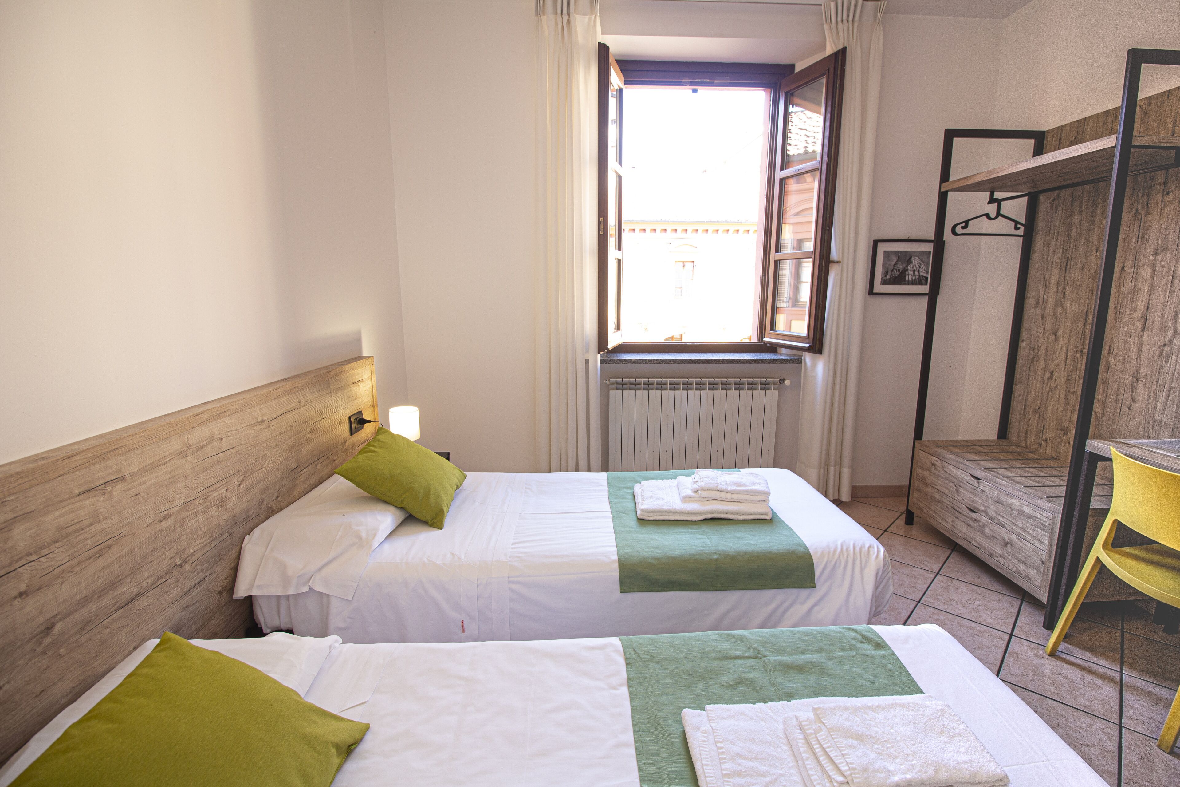 A hotel room with two beds, a window with curtains, a radiator, and a wooden headboard.