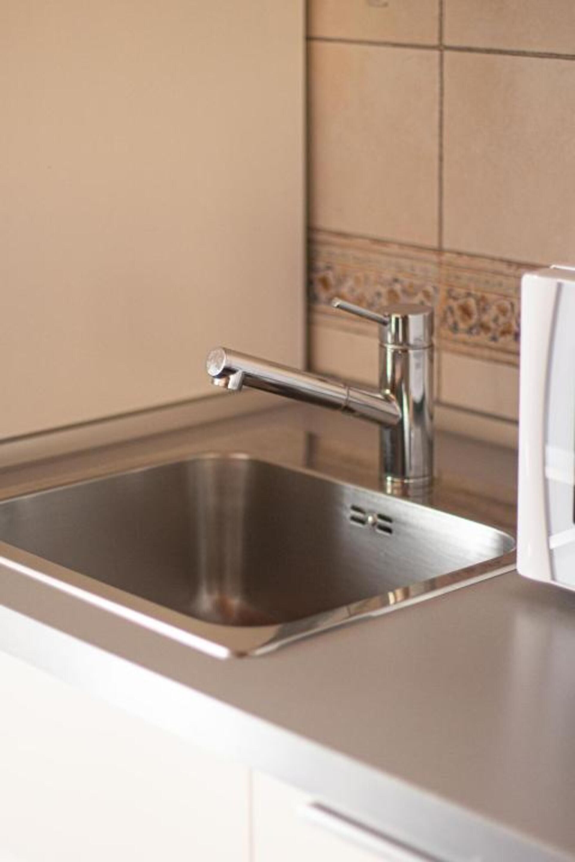 Un lavamanos de acero inoxidable con un grifo moderno, una encimera blanca y un salpicadero de azulejos.