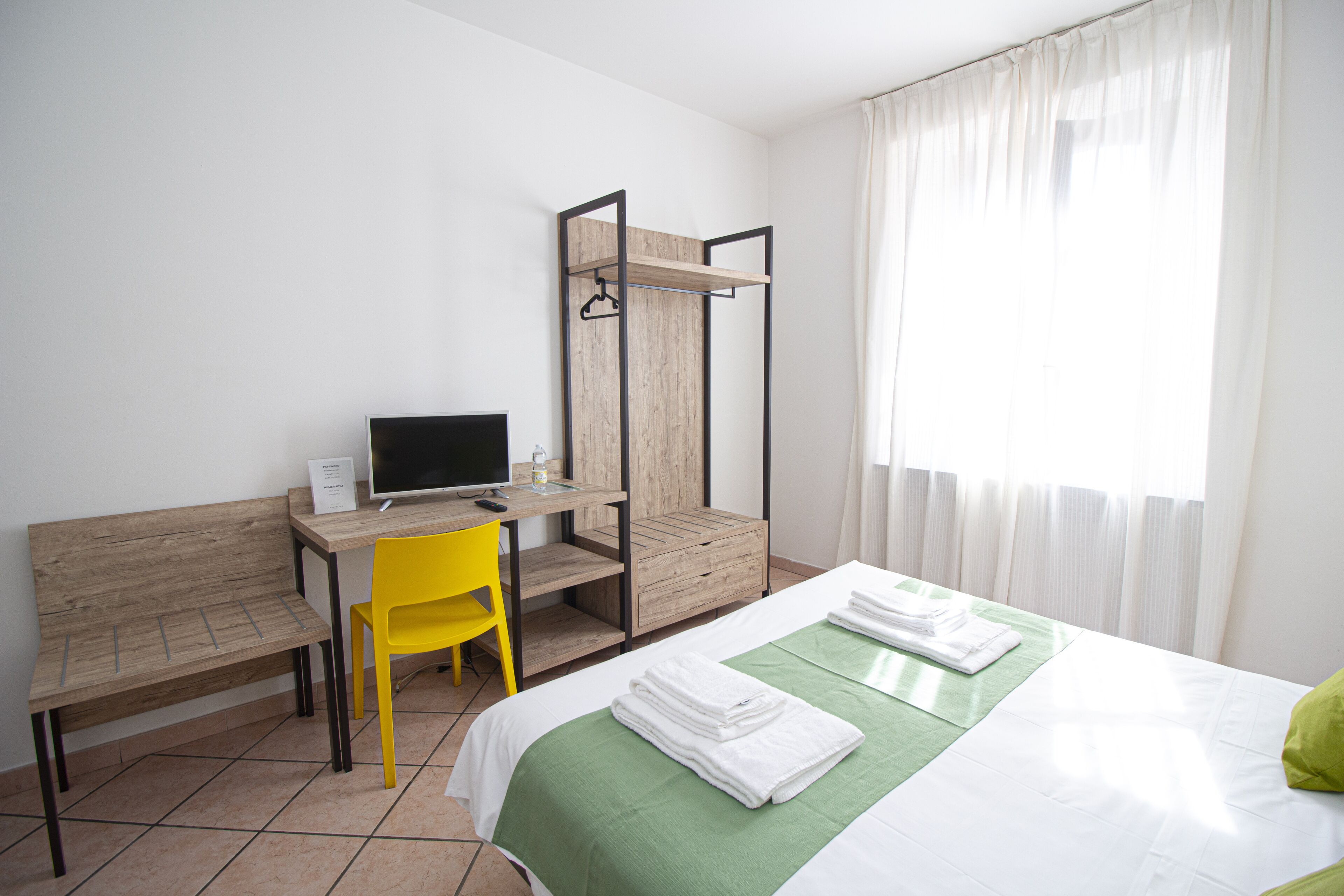 Une chambre d’hôtel avec un lit, un bureau avec un ordinateur, une chaise et un banc en bois.