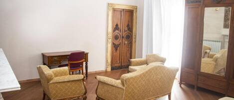 A room with a wooden floor, a desk with a chair, two armchairs, a dresser, and a mirror.