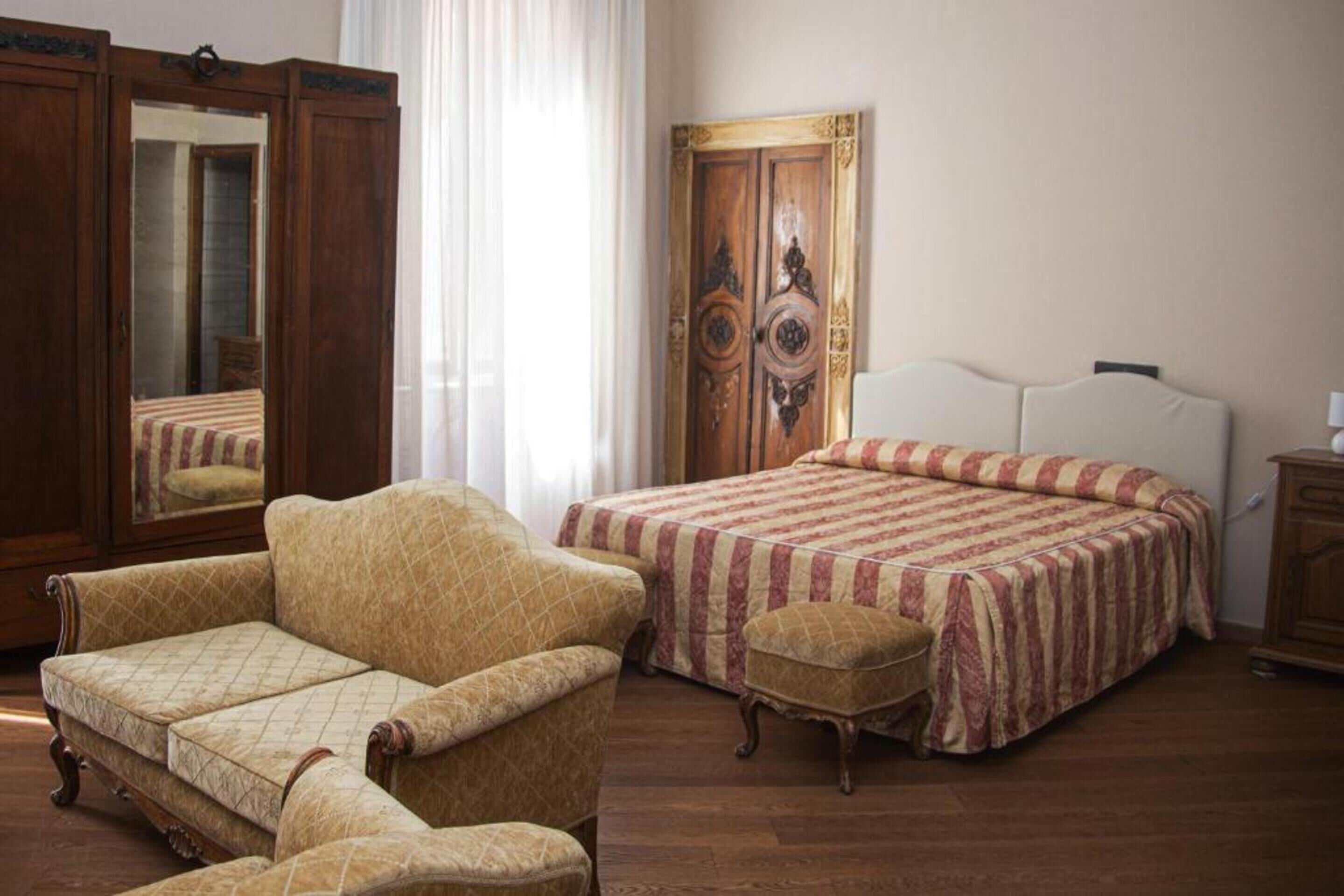 Un dormitorio con cama, una silla, una mesita, un armario y un espejo.
