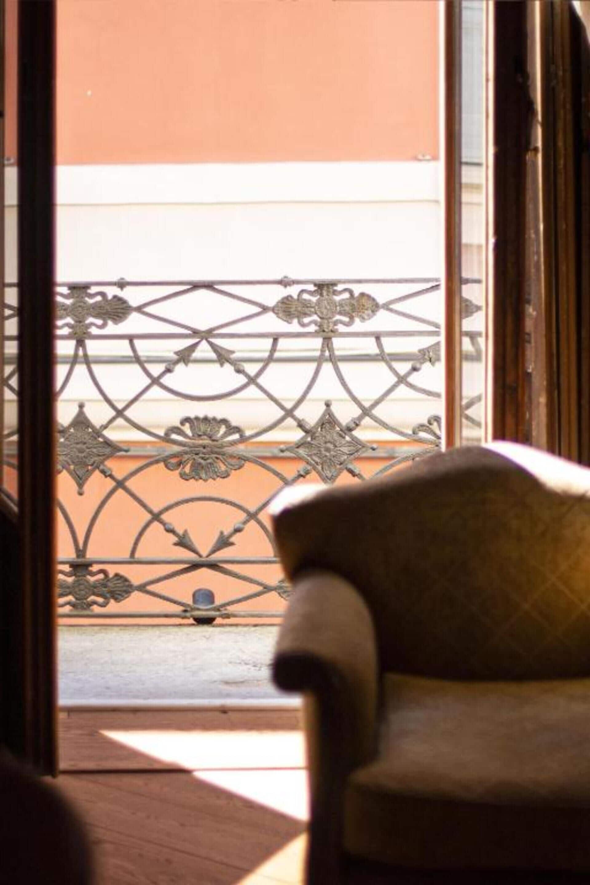 Una sedia in una stanza con vista su un balcone con ringhiere in metallo decorate.