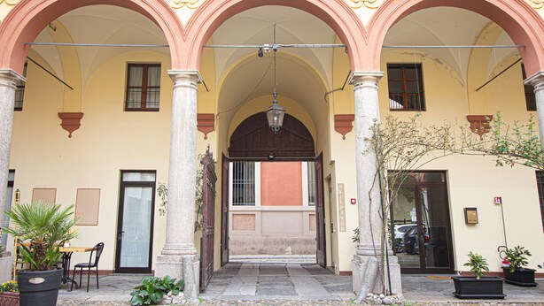 Un edificio con un patio cubierto, que cuenta con arcos, columnas y plantas en macetas.
