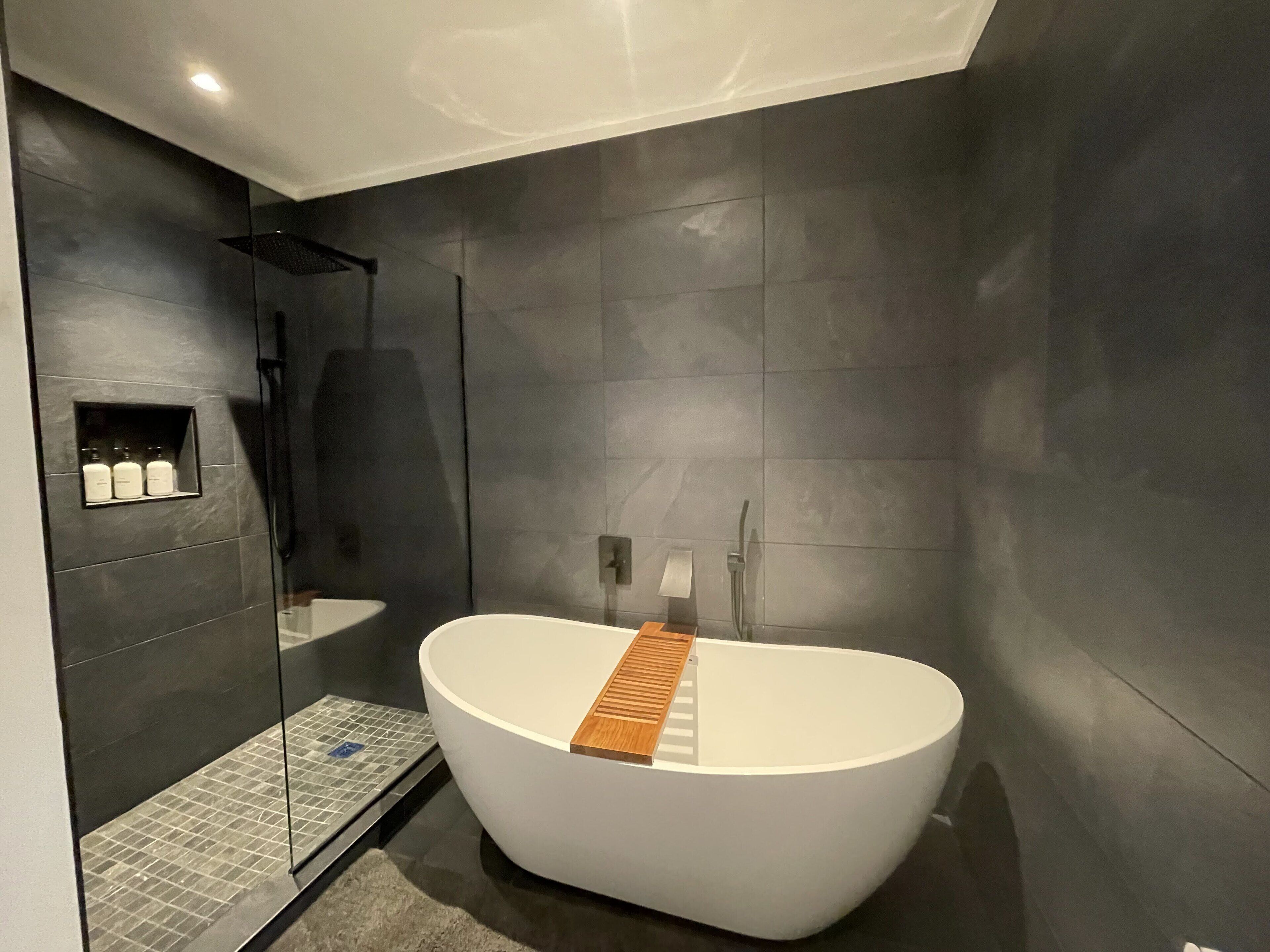 A modern bathroom with a freestanding bathtub, a glass shower enclosure, and a built-in shelf with toiletries.