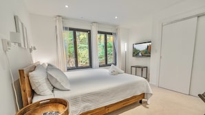 A bedroom with a wooden bed, white bedding, a wooden side table with a remote, and a TV on the wall. - Scandi Lakefront Stay w/ Free Pool & Club Passes (Lake Harmony)