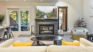 A modern living room with a fireplace, a dining area, and a large window with a view of trees. - Scandi Lakefront Stay w/ Free Pool & Club Passes (Lake Harmony)