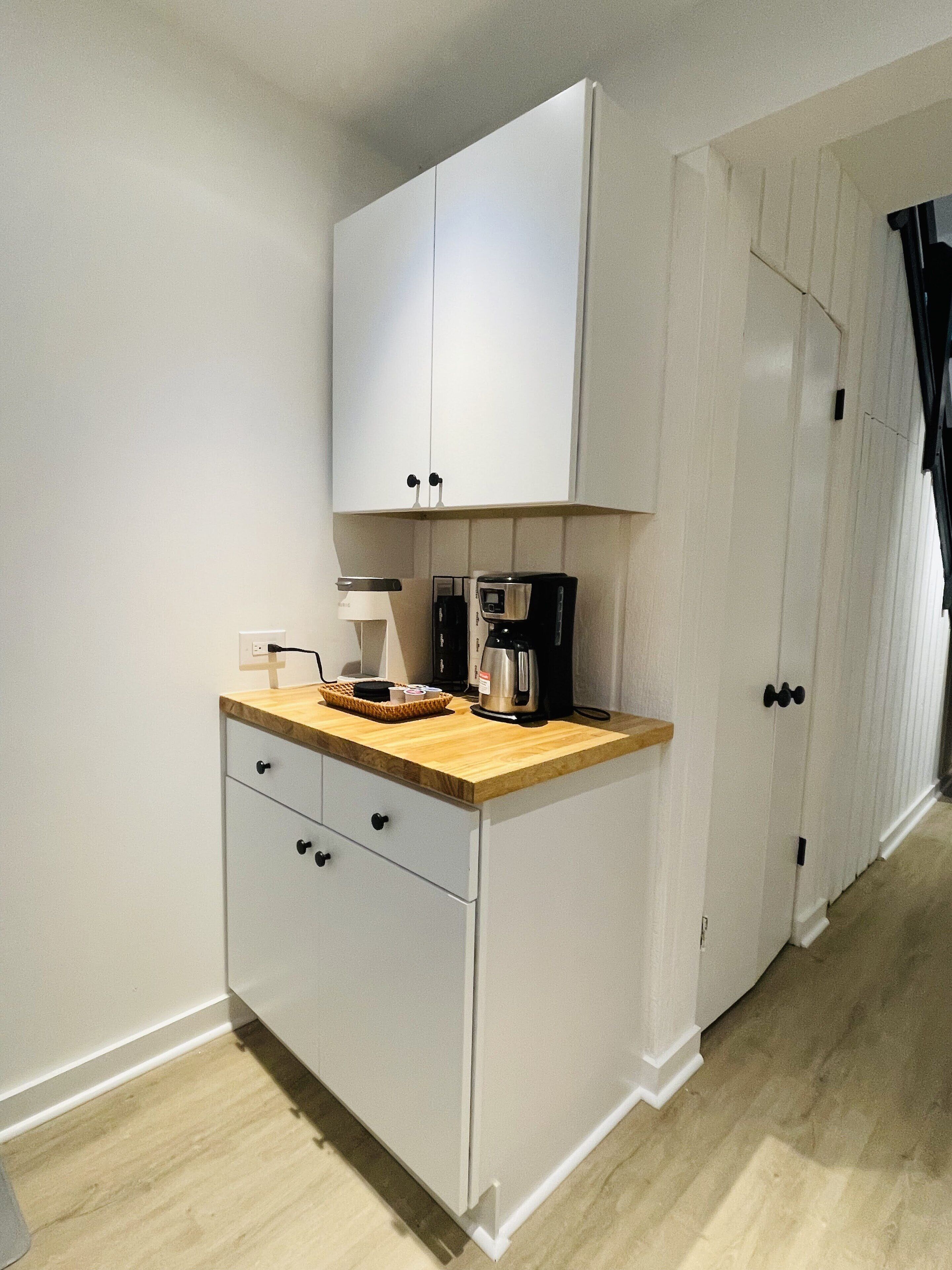 A compact kitchen with white cabinets, a wooden countertop, and a coffee maker.