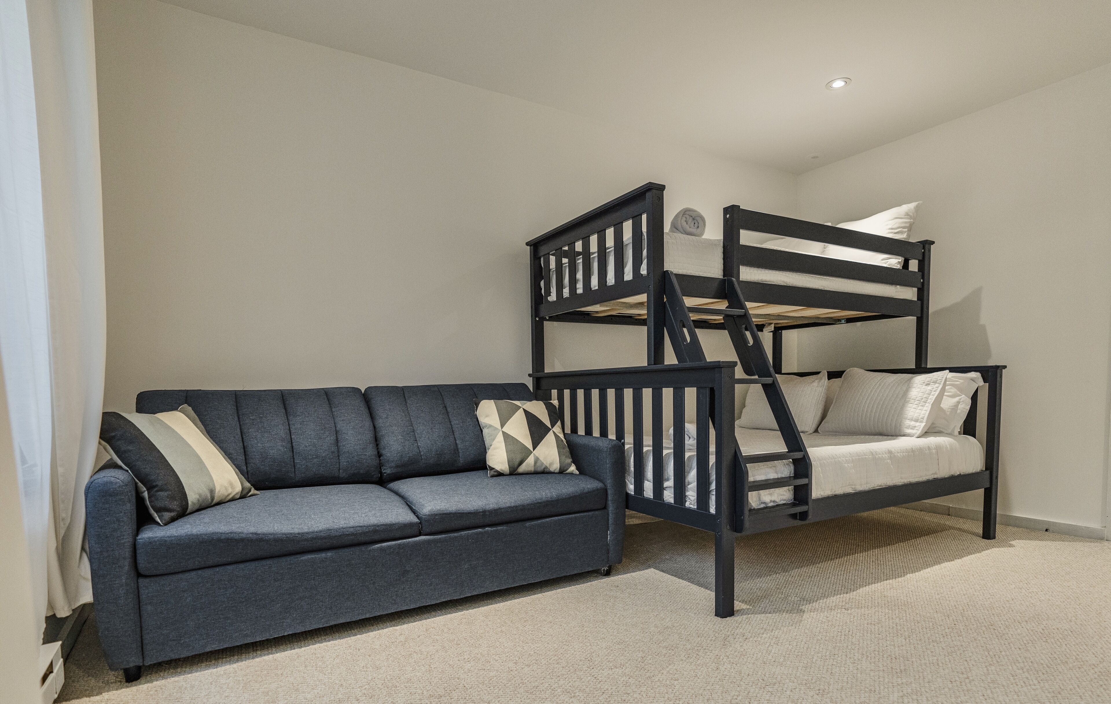 A room with a bunk bed, a sofa, and a carpeted floor.