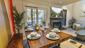 A dining area with a wooden table set for four, a fireplace, and a large window with a view of trees. - Scandi Lakefront Stay w/ Free Pool & Club Passes (Lake Harmony)