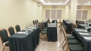 Une salle de conférence avec des rangées de tables, de chaises et des bouteilles d’eau.