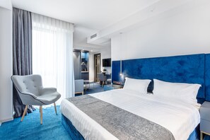 Une chambre d’hôtel moderne avec un grand lit, un fauteuil gris et un espace bureau.
