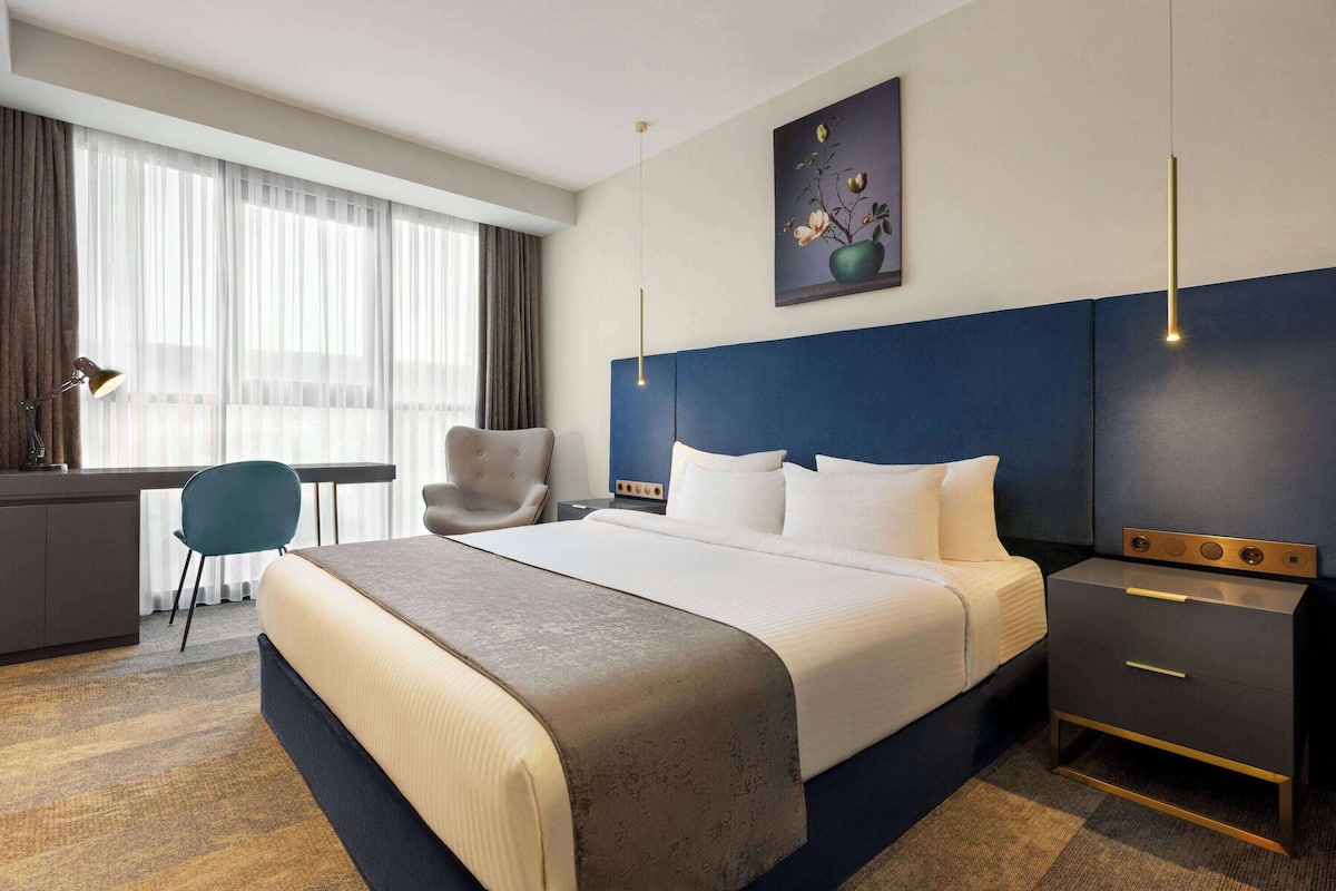 A hotel room with a large bed, a desk, a chair, and a nightstand.
