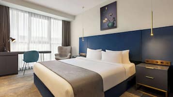 A hotel room with a large bed, a desk, a chair, and a nightstand.