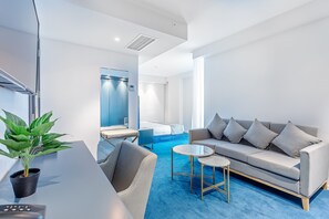 A modern hotel room with a grey sofa, a small round table, a potted plant, and a blue carpet. - Ramada by Wyndham Tbilisi Old City (Tbilisi)