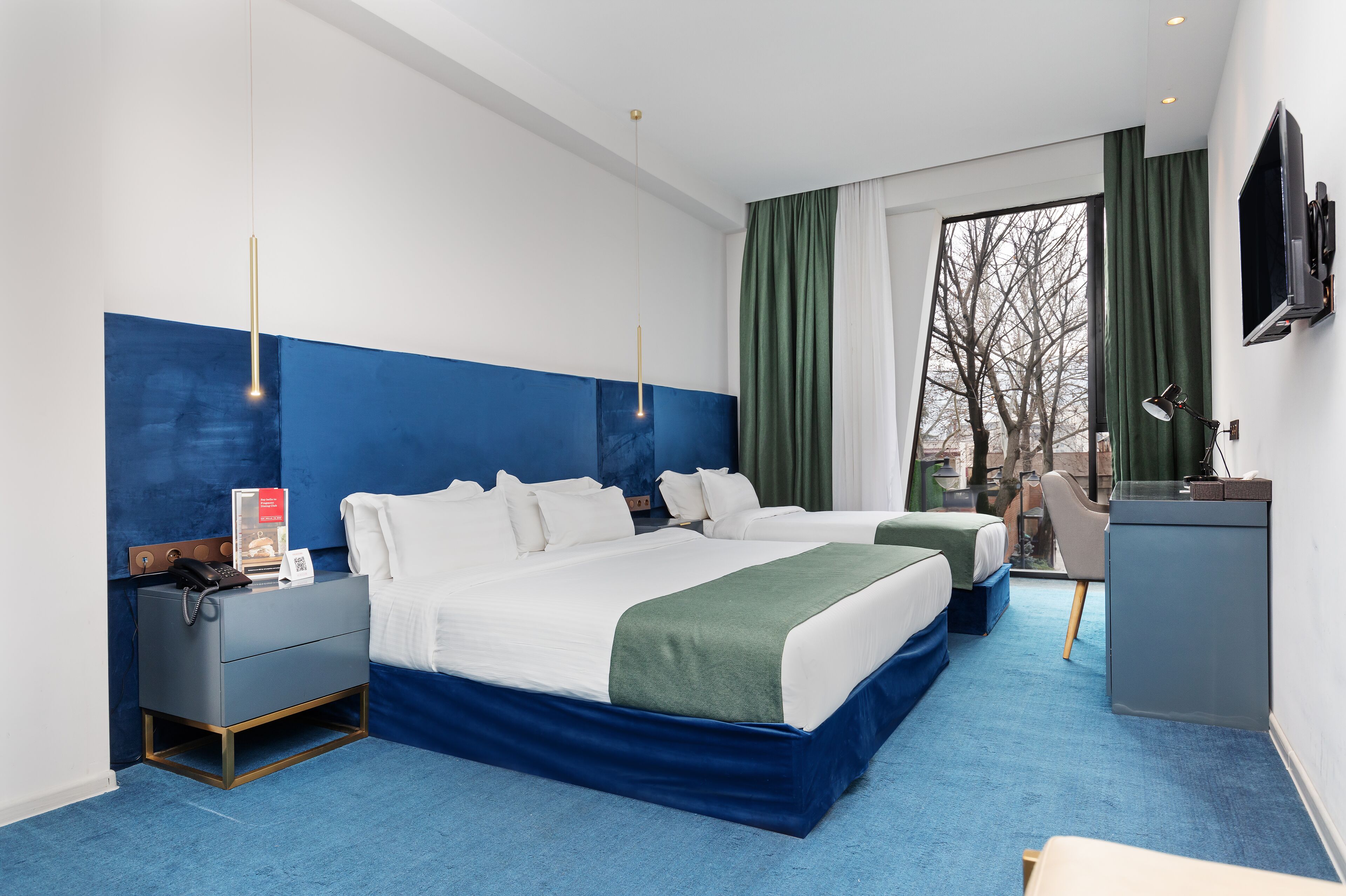 A hotel room with two beds, a desk, a TV, and a window with curtains.