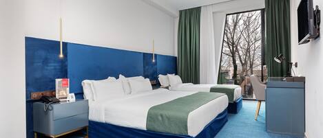 A hotel room with two beds, a desk, a TV, and a window with curtains.