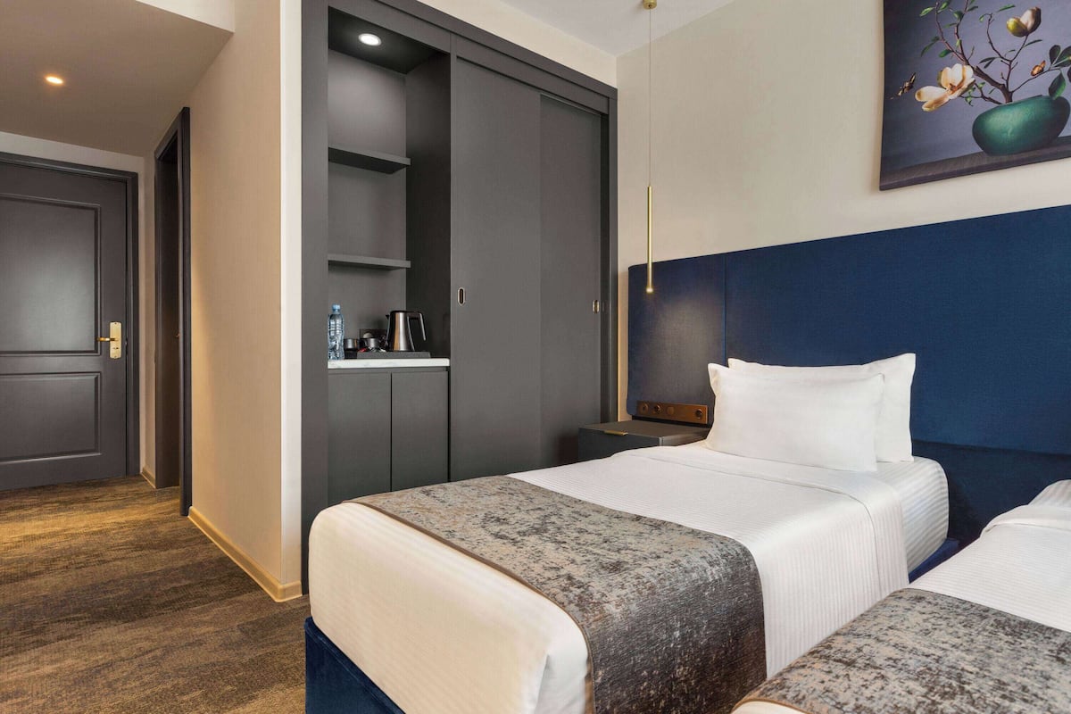 A hotel room with a large bed, a wardrobe, a small desk with a lamp, and a painting on the wall.