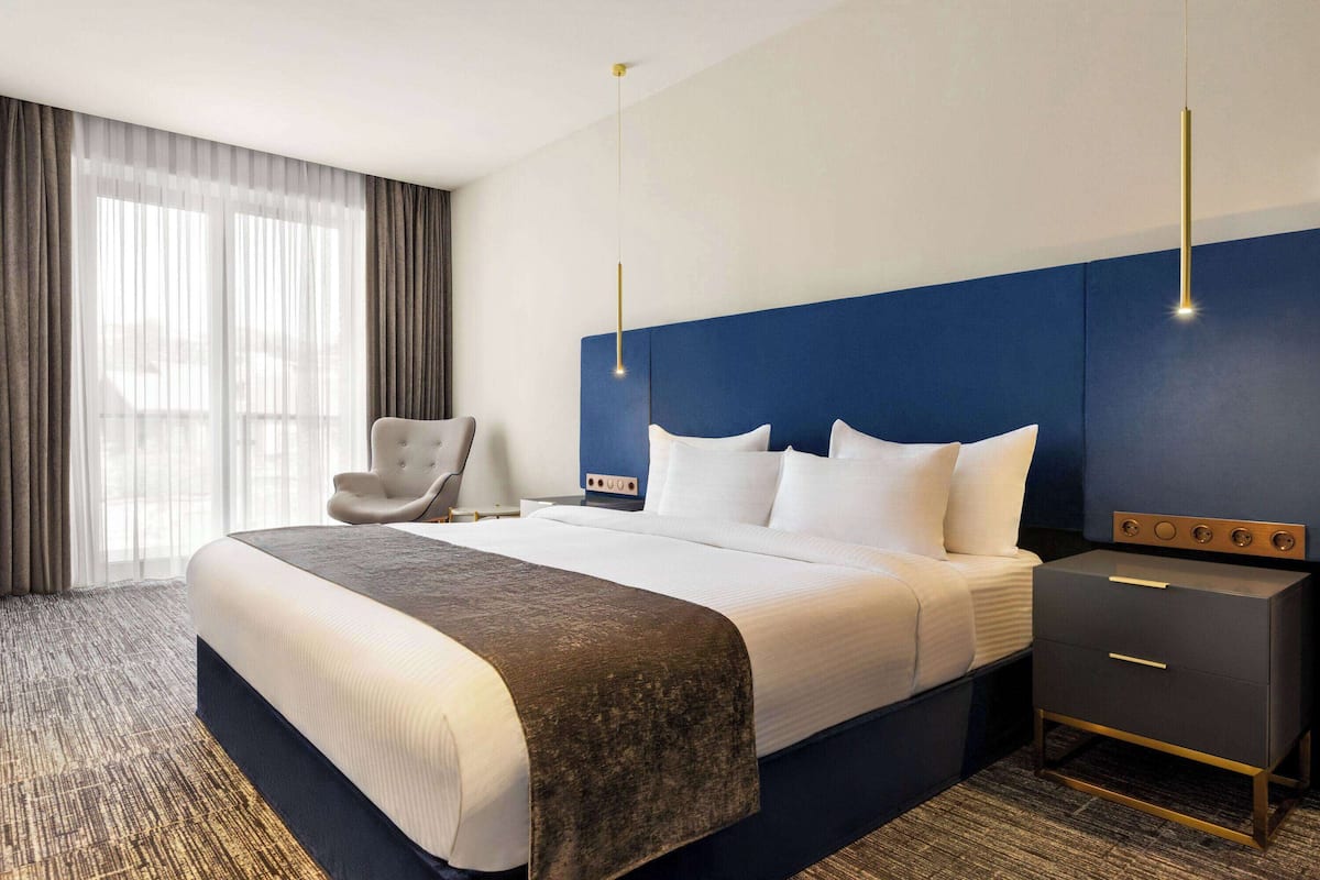 A hotel room with a large bed, a bedside table, a chair, and a nightstand.