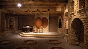 Een rustiek interieur met stenen muren, houten balken en een centrale zithoek met stoelen en een tafel.