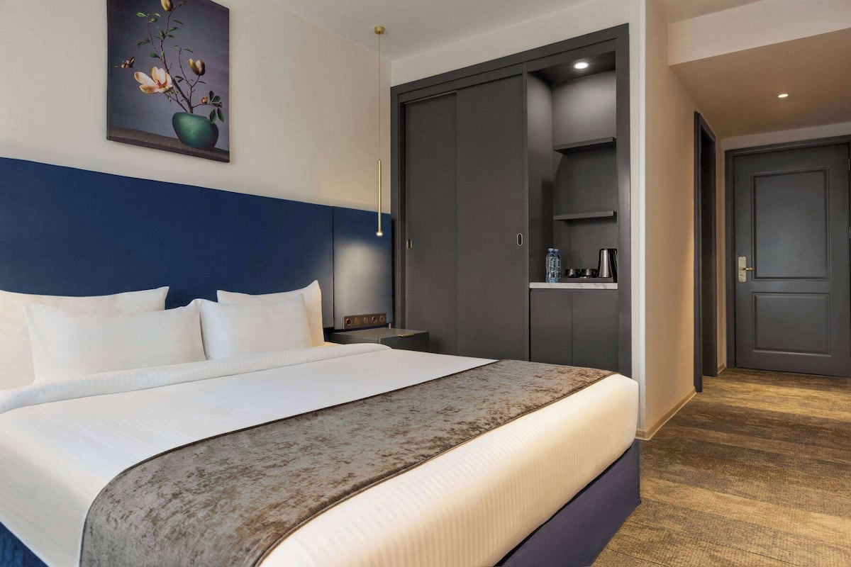 A hotel room with a large bed, a nightstand, a dresser, a wardrobe, and a painting on the wall.